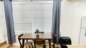 Un comedor con una mesa y sillas de madera, una planta en maceta y un cubo de basura negro.