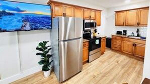 A modern kitchen with wooden cabinets, stainless steel appliances, and a large flat-screen TV mounted on the wall.