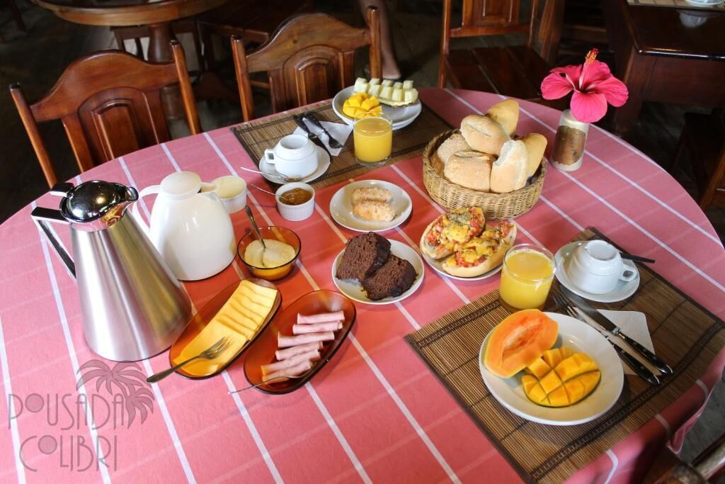 Una mesa de desayuno con diversos alimentos, una cafetera y un florero.