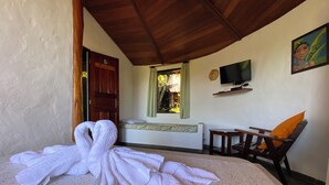 A room with a bed, a wooden ceiling, a TV, a painting, and a chair with an orange cushion. - Pousada Colibri (Cairu)