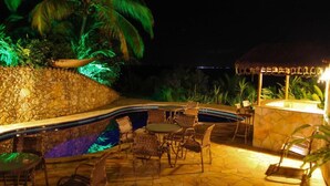 A nighttime outdoor pool area with stone walls, wicker furniture, and a thatched-roof structure. - Pousada Colibri (Cairu)