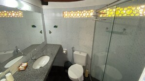 A bathroom with a granite countertop, a white sink, a toilet, and a glass-enclosed shower. - Pousada Colibri (Cairu)