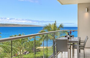 Uma varanda com vista para o oceano, uma mesa com cadeiras e uma garrafa de vinho.