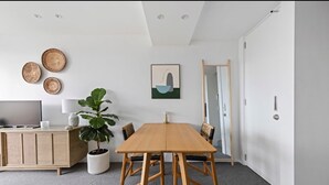 A modern living room with a wooden dining table, a TV, and a cabinet. - THE LITTLE BEACHSIDE APARTMENT  (Manly)