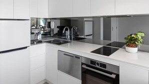 A modern kitchen with white cabinetry, a built-in dishwasher, a double sink, and a stainless steel range hood. - THE LITTLE BEACHSIDE APARTMENT  (Manly)