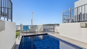 A rooftop swimming pool with a clear view of the city skyline, surrounded by a metal railing and a solar panel. - THE LITTLE BEACHSIDE APARTMENT  (Manly)