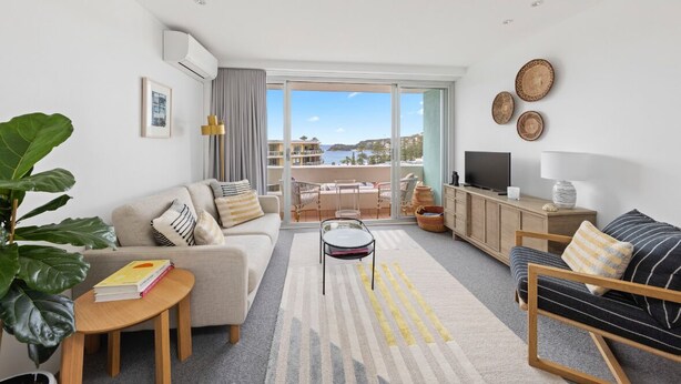 A modern living room with a sofa, a coffee table, a TV, and a view of the sea. - THE LITTLE BEACHSIDE APARTMENT  (Manly)