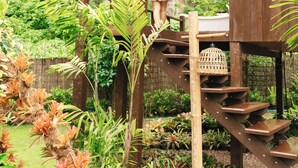A wooden structure with a staircase, surrounded by lush greenery and a cliff in the background.