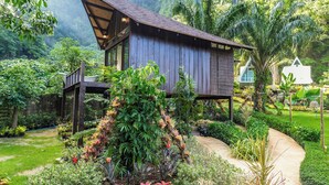 A wooden house elevated on stilts surrounded by lush greenery and a garden path.