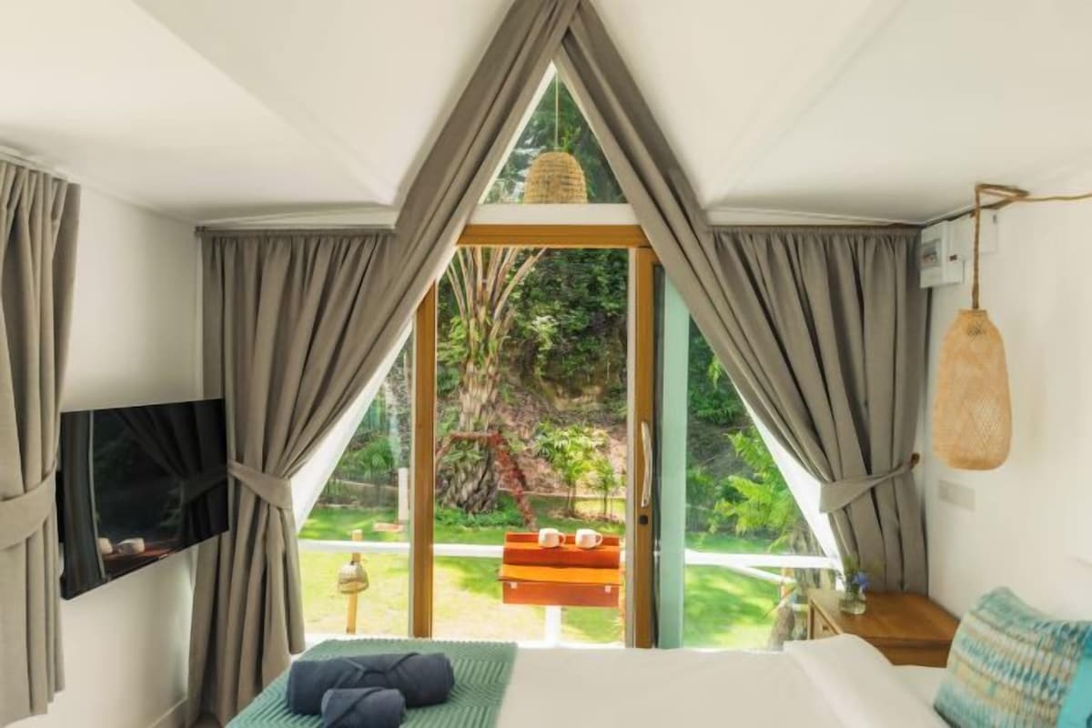 Un dormitorio con una cama, televisión y vistas a un jardín a través de un ventanal.