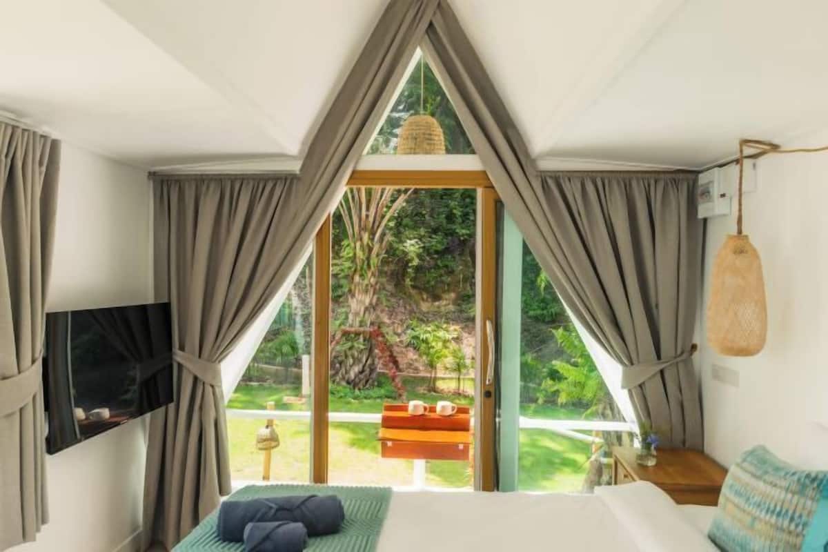 Ein Schlafzimmer mit Bett, Fernseher und Blick auf einen Garten durch eine Glastür.