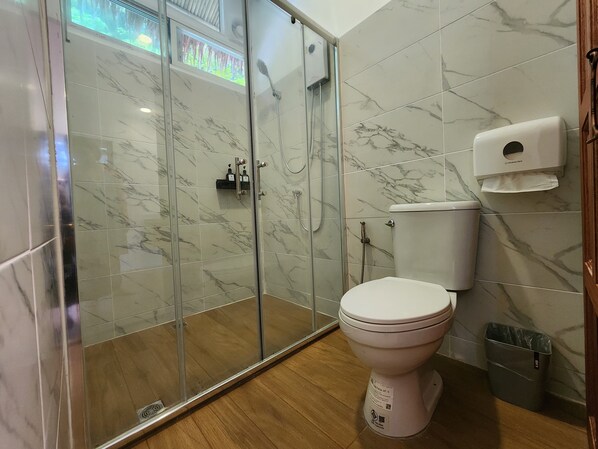 A bathroom with a glass-enclosed shower, a toilet, and a paper towel dispenser.