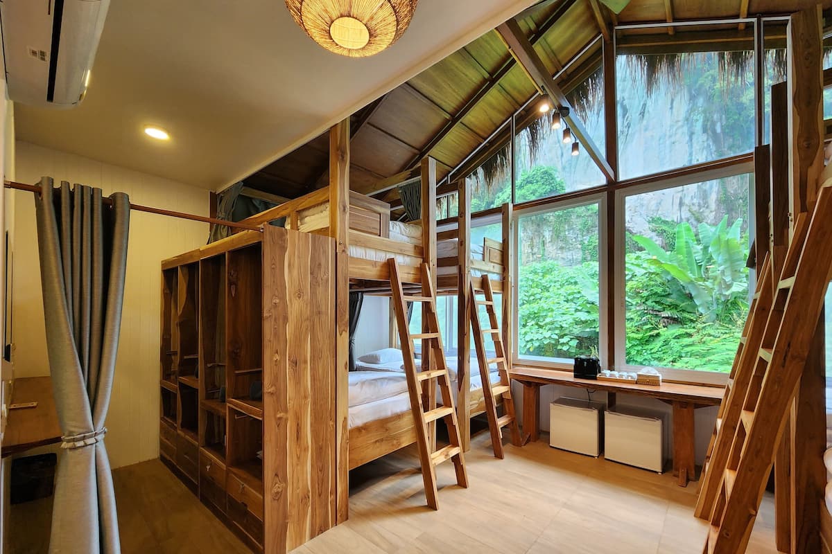 Ein Zimmer mit einem Etagenbett, einer Holzleiter und großen Fenstern mit Blick auf Grünflächen.