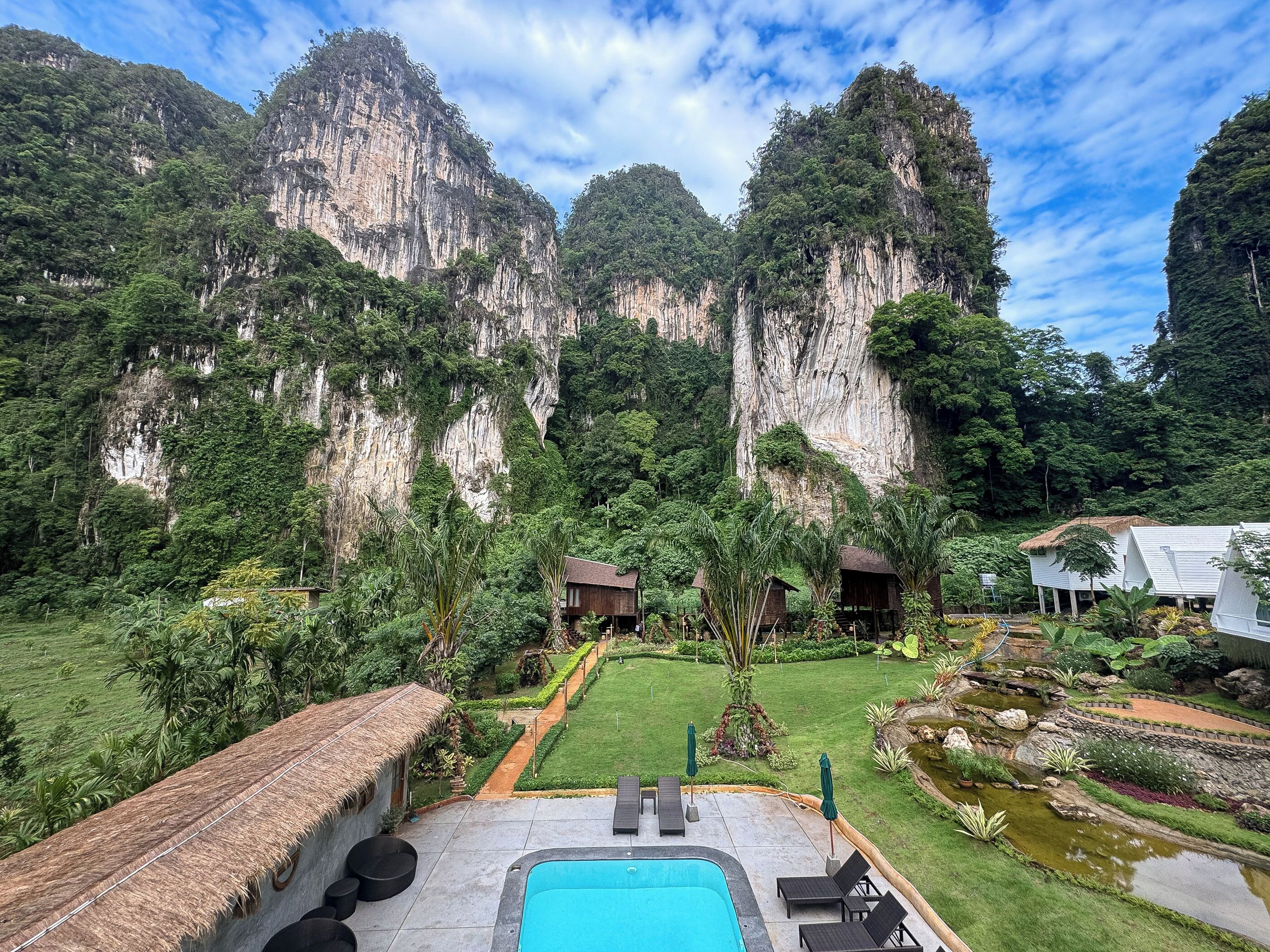 Un complexe hôtelier doté d'une piscine, de bâtiments à toits de chaume et d'un jardin luxuriant offrant une vue imprenable sur d'imposantes falaises.