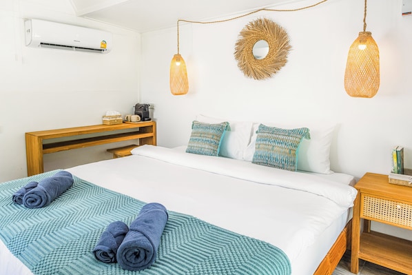A neatly made bed with a teal and white bedspread, two rolled towels, and a wooden nightstand with a wicker basket. - Voasis Valley Krabi - Natural Resort - Adults Only (Krabi)