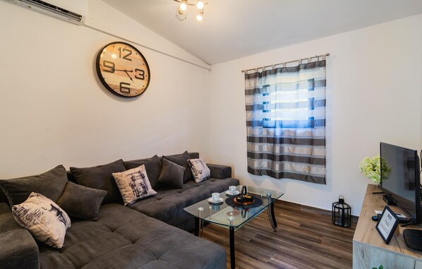 A modern living room with a sofa, a glass coffee table, a clock, a striped curtain, a TV, and a small plant. - Stunning home in Dol Postira with WiFi (Dol Postira)