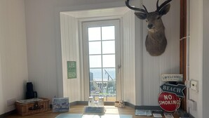 A reception desk with a mounted deer head, a window with a view of the beach, and a 'No Smoking' sign. - Unique house in an idyllic situation on a beach (Port Ellen, Isle of Islay)