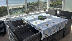 A sunlit room with a table set for two, overlooking a coastal view. - Unique house in an idyllic situation on a beach (Port Ellen, Isle of Islay)