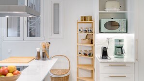 Una cocina moderna con armarios blancos, microondas, cafetera y un estante de madera para especias.