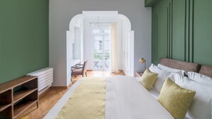 Un dormitorio con una cama grande, una mesita de noche de madera, una silla y vistas al balcón exterior.