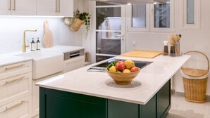 Una cocina moderna con gabinetes blancos, una isla central con un cuenco de fruta y una campana extractora de acero inoxidable.