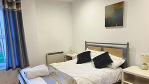 Habitación de hotel ordenada con cama, mesitas de noche, un radiador y un cuadro en la pared.