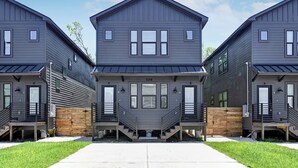 Een rij moderne, grijze woningen met twee verdiepingen, een centrale ingang en een houten hek.