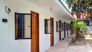 Un couloir avec des portes et des fenêtres, un ventilateur de plafond et un petit espace jardin avec des plantes.
