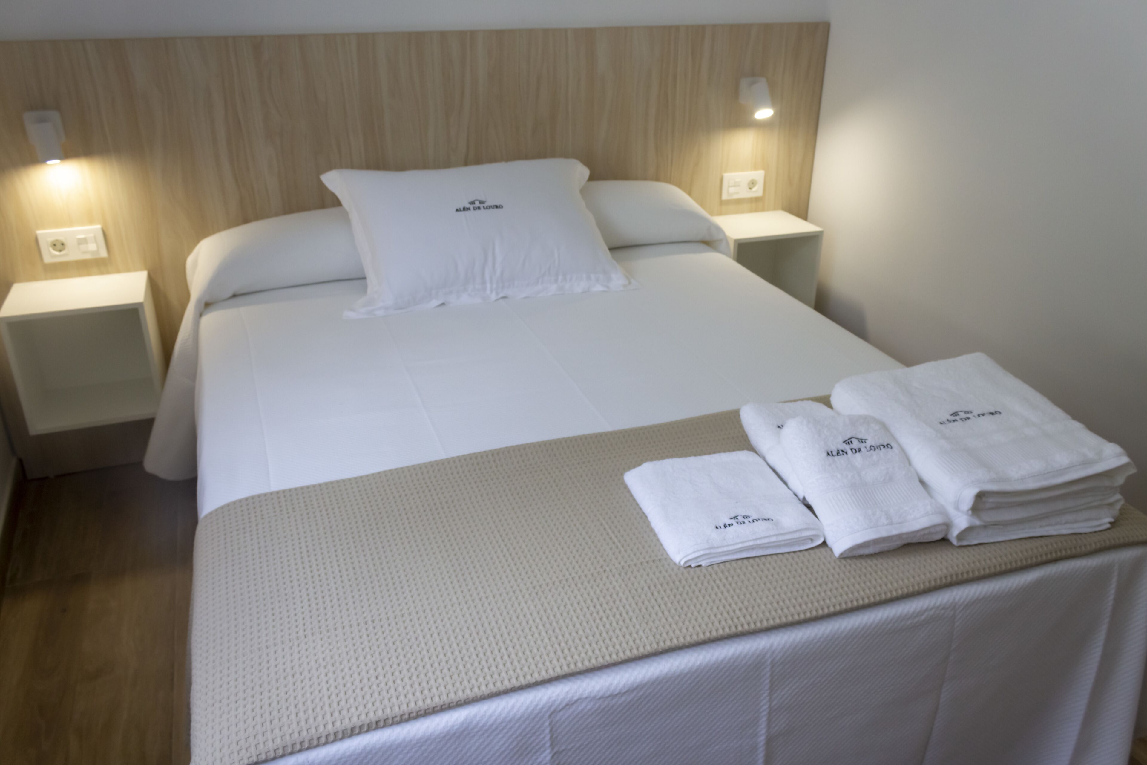 Un lit bien fait, avec des draps blancs, deux lampes de chevet et une pile de serviettes pliées posée sur le lit.