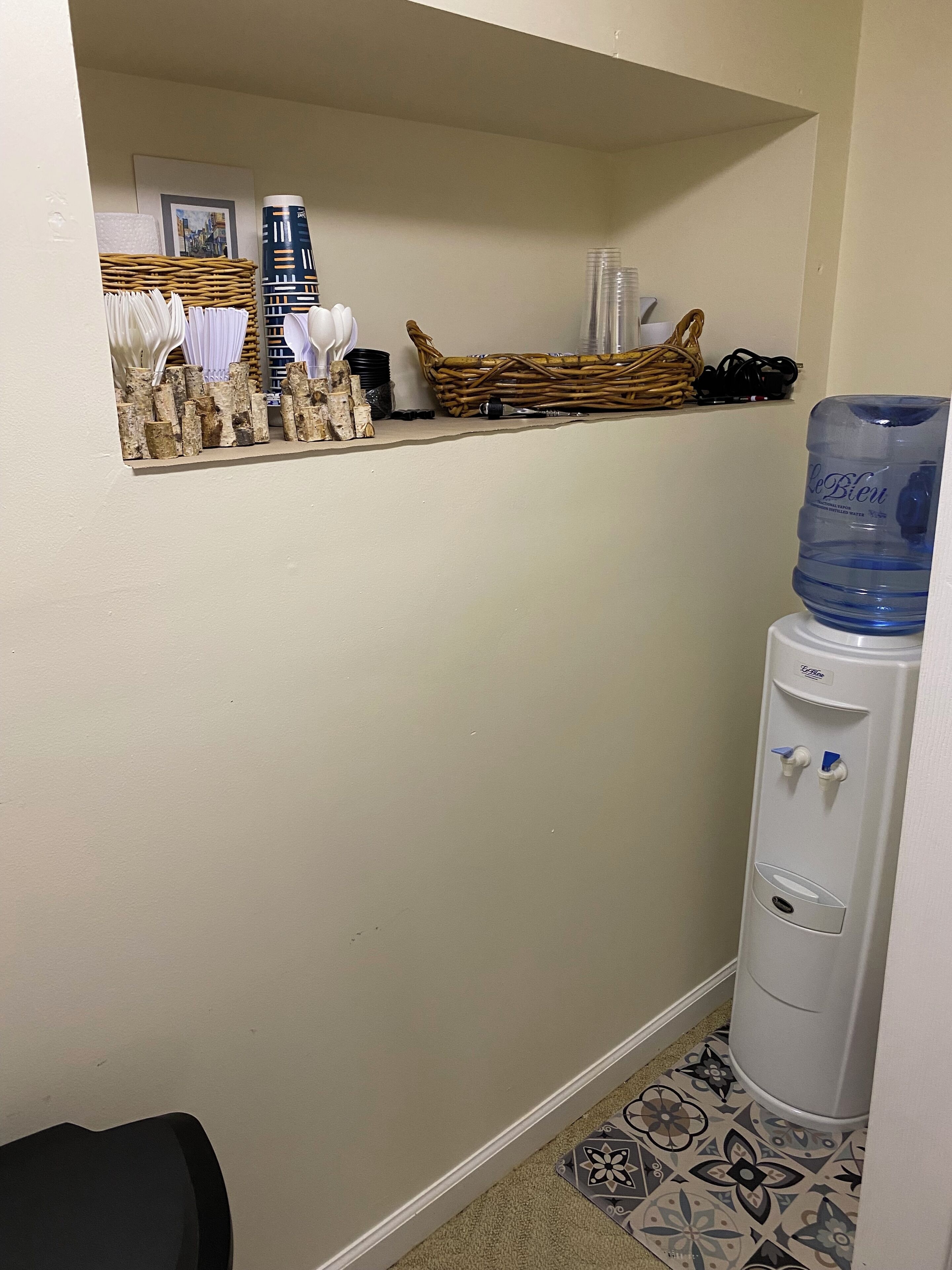 Une petite salle de bain fermée, équipée d’un distributeur d’eau, d’un panier en osier et d’un tableau encadré accroché au mur.