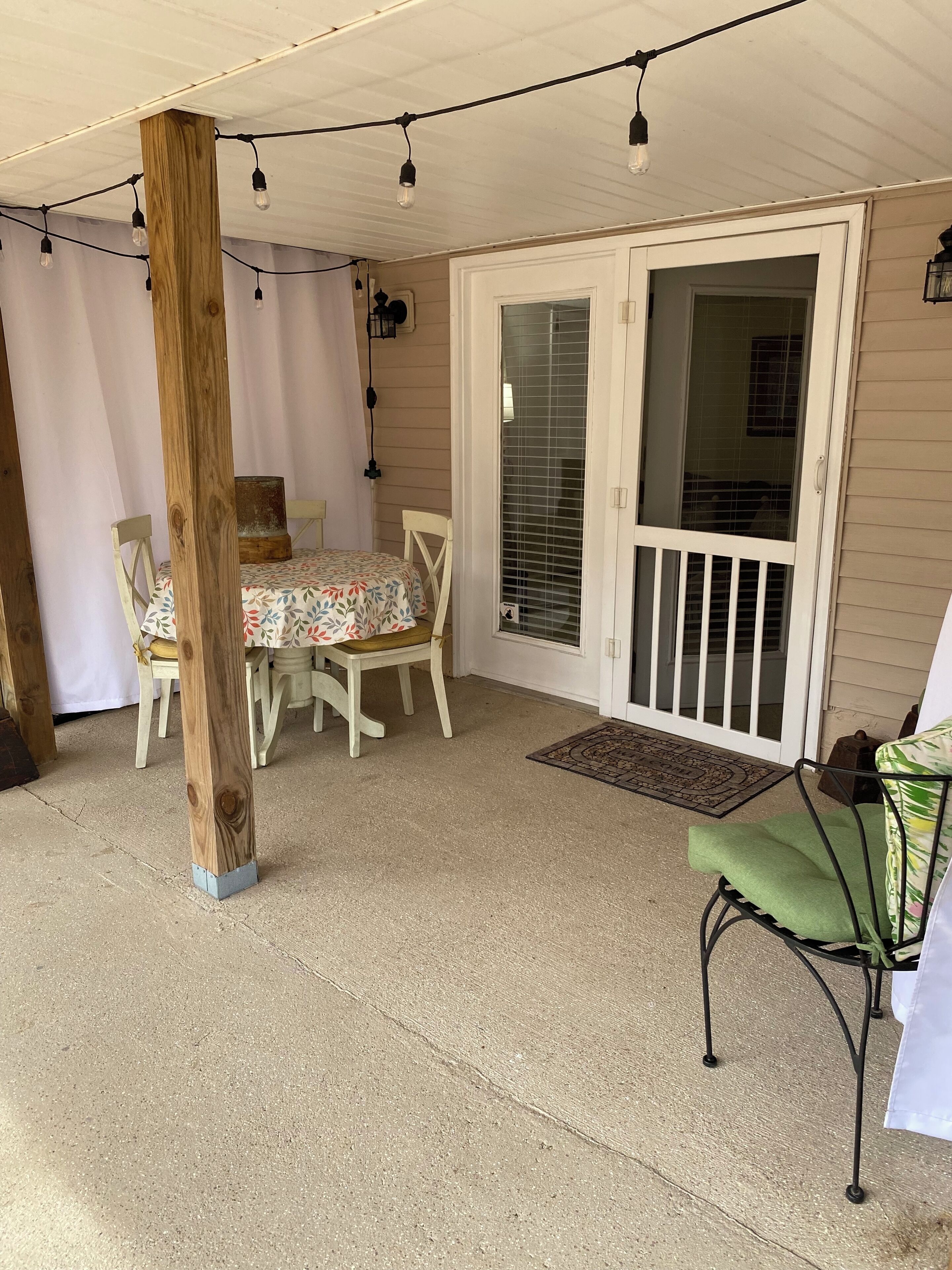 Une terrasse couverte avec une table et des chaises, un poteau en bois et une porte-fenêtre coulissante.