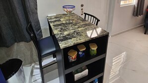 Un área de comedor con una mesa, sillas, un cuenco de vidrio y una repisa con recipientes.