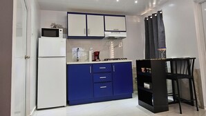 Una cocina compacta con armarios blancos y azules, microondas, cafetera y estufa a gas.
