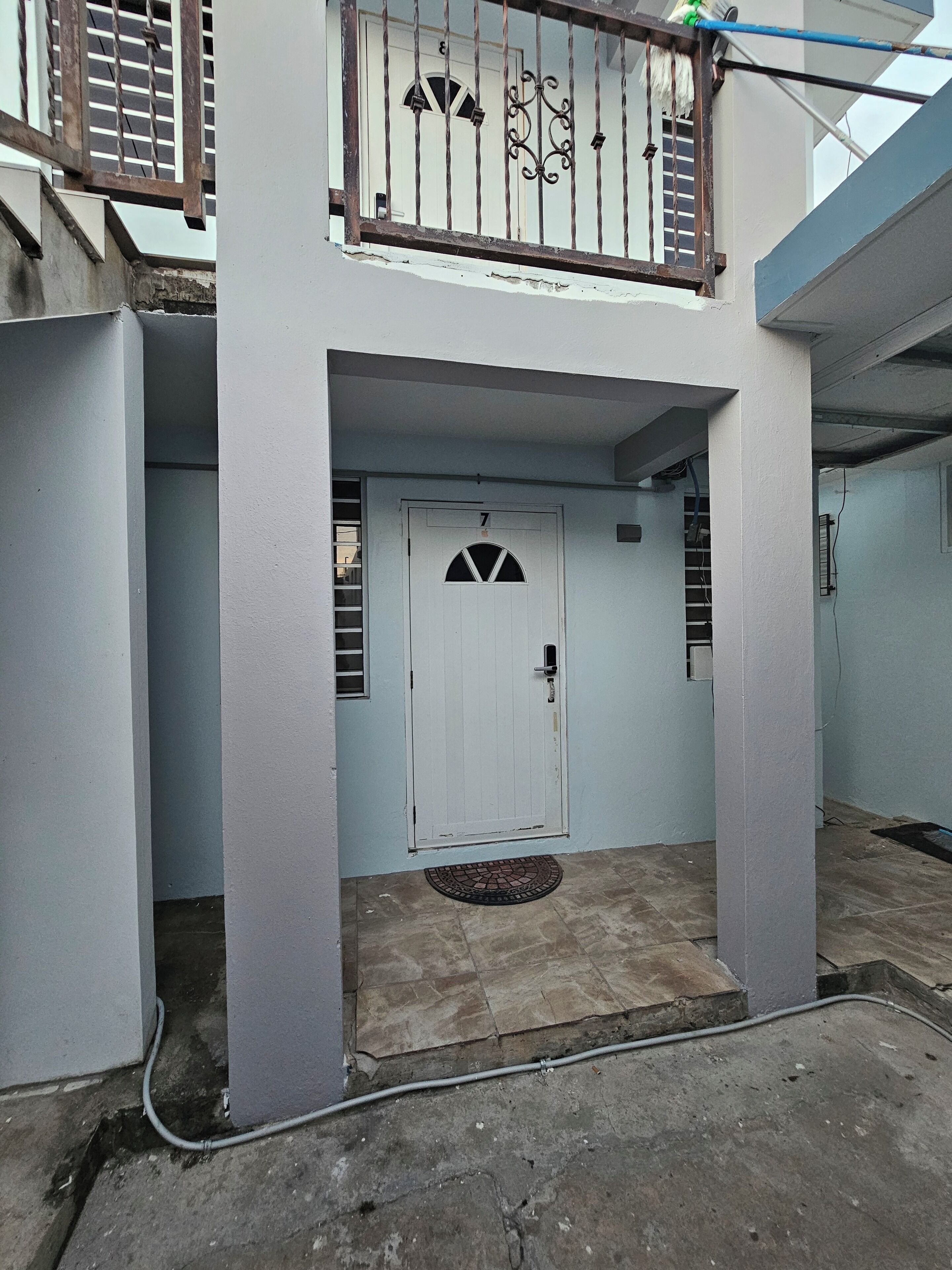 Una puerta blanca con el número 7, una ventana pequeña y una reja de metal.