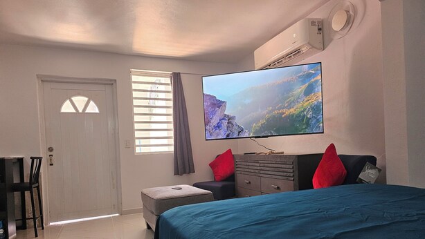 Un dormitorio con una cama, un televisor montado en la pared, un aparador y una ventana con persianas.