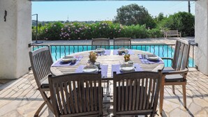 Mesa de madera preparada para cuatro personas, con sillas, con vistas a una piscina y a la vegetación y colinas.