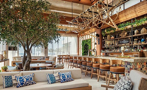 A spacious lounge area with a large tree, wooden furniture, and a bar with shelves of bottles.