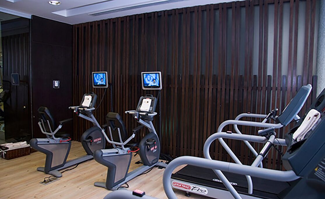 Une salle de sport équipée de plusieurs tapis de course et vélos d’appartement, avec des murs recouverts de panneaux de bois et deux écrans fixés au mur.