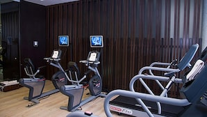 Un gimnasio con cintas de correr y bicicletas estáticas, paredes de paneles de madera y dos monitores en la pared.