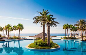 A resort pool area with palm trees and a view of the ocean.