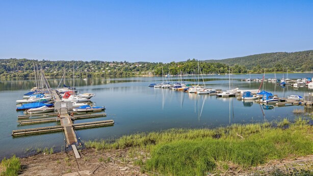 Un port de plaisance où sont amarrés des bateaux, entouré de verdure et de collines.
