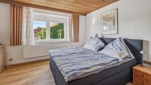 Une chambre à coucher avec un lit, une fenêtre avec des rideaux, un radiateur et un tableau encadré au mur.