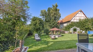 Un jardin avec un kiosque, un barbecue et une serre.