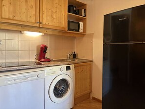Una cucina compatta con lavatrice, forno a microonde e frigorifero nero.