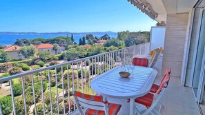 Un balcon avec une table et des chaises, donnant sur un paysage côtier avec des maisons et des arbres.