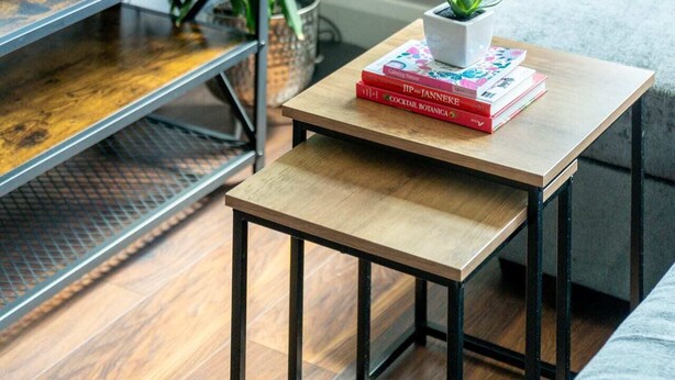 A modern living room with a wooden coffee table, a television on a shelf, a floor lamp, and a large green plant.