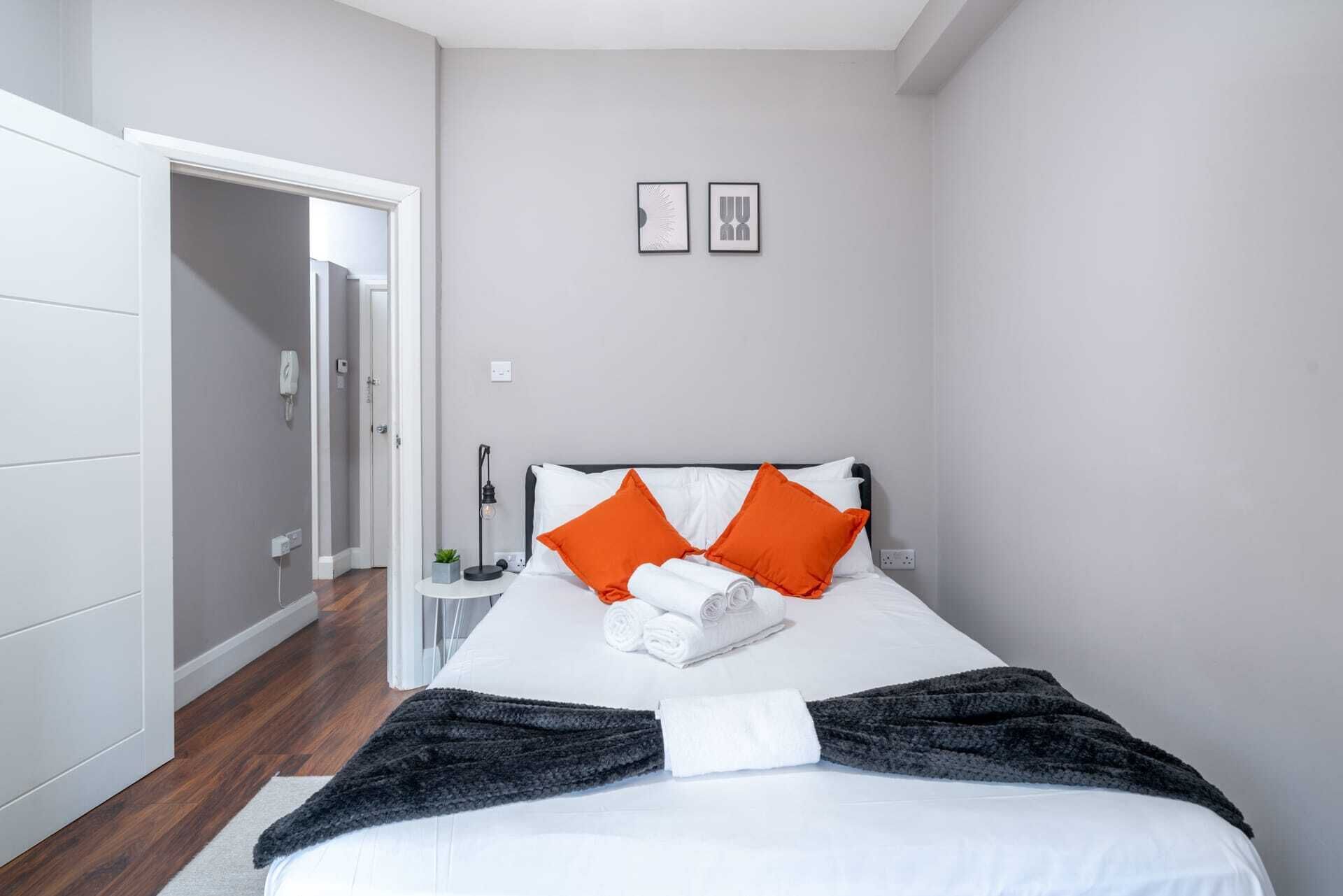 Quarto com cama, almofadas, mesa de cabeceira e luminária na parede.