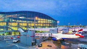 A modern airport terminal with glass facade, multiple aircraft parked, and a clear sky.
