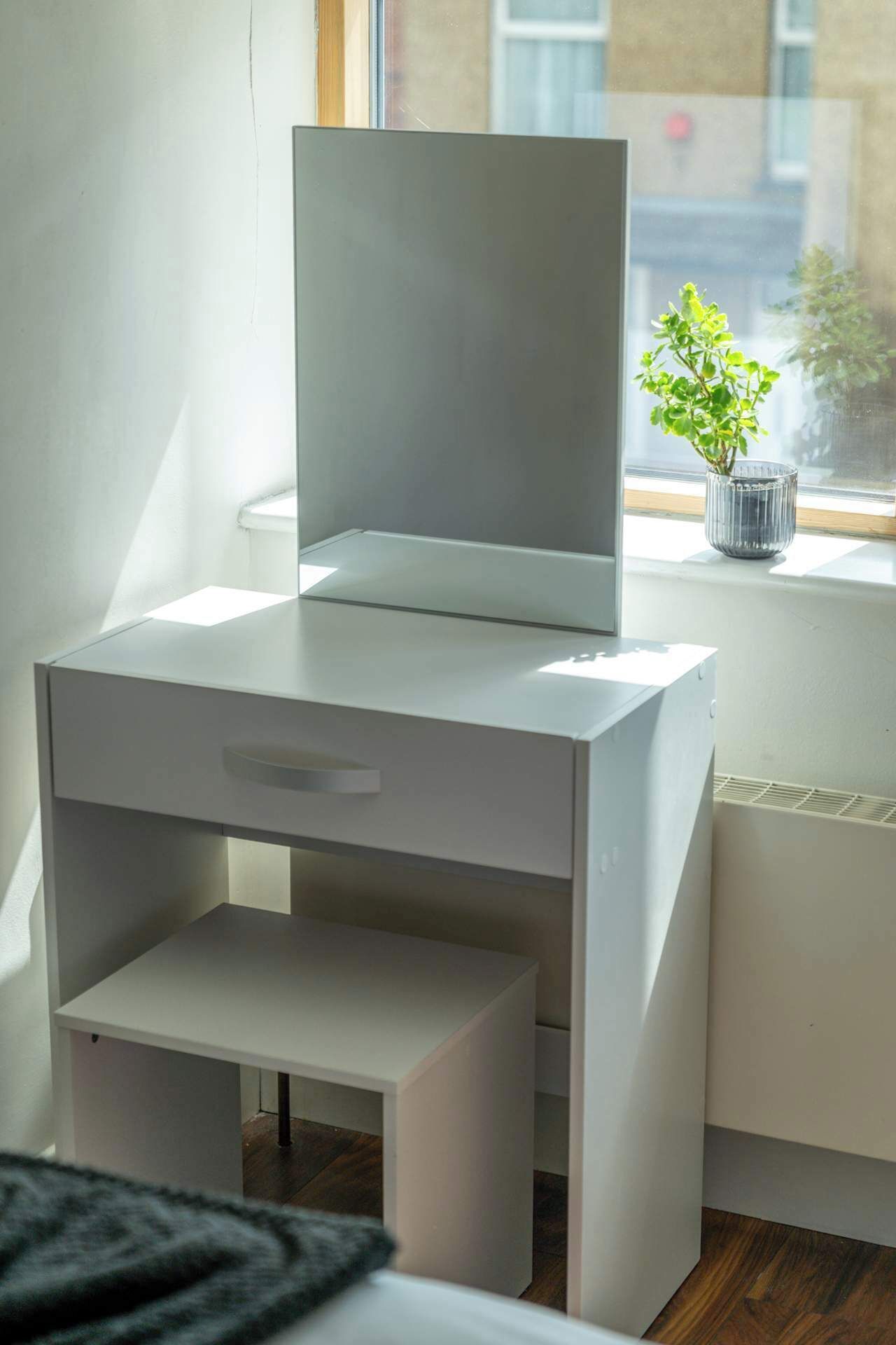 A modern, minimalist room with a white bedside table, a small drawer, and a window with a view of buildings.