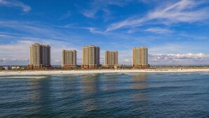 A beachfront hotel with multiple high-rise buildings, a sandy beach, and a clear blue sky.